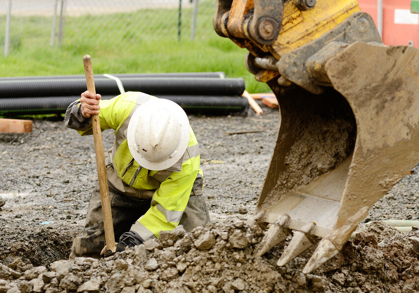 Worker using a small tracked excavator to dig a hole to fix a water leak at a large commercial housing development in Oregon